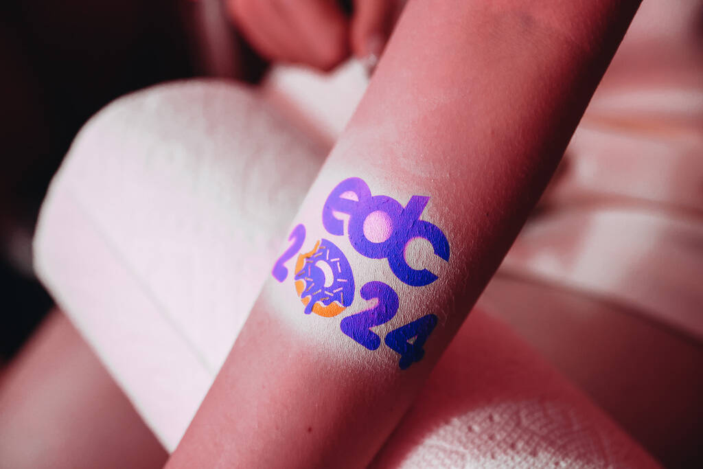 A festival attendee receives an airbrush tattoo inside of a Dunkin’ Donuts themed pop up ...