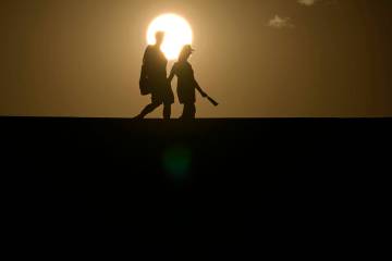 People walk along a trail as the sun sets, Sunday, July 16, 2023, in Death Valley National Park ...