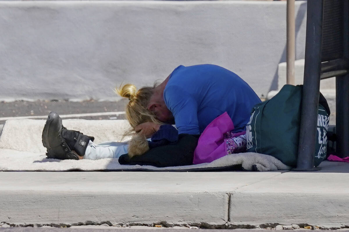 With hands covering their forehead, a person waits at a bus stop as temperatures are expected t ...