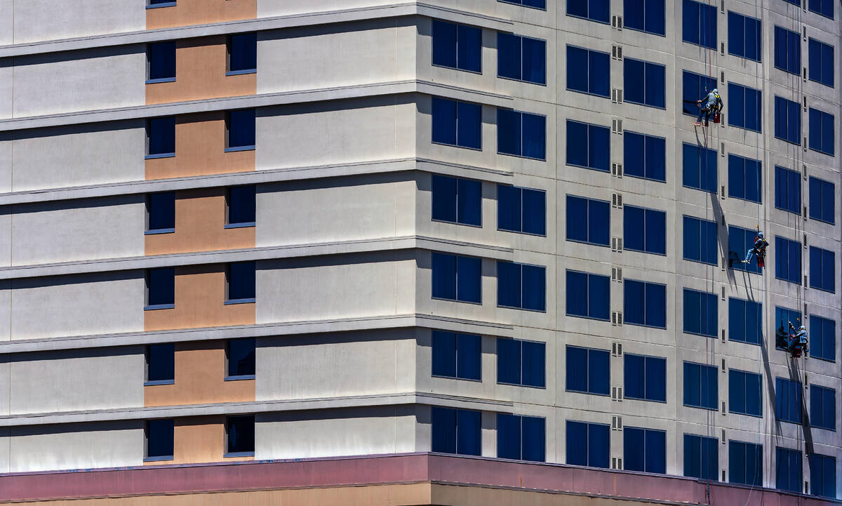 Window washers scale down the exterior of the Club Wyndham Grand Desert as workers use protecti ...