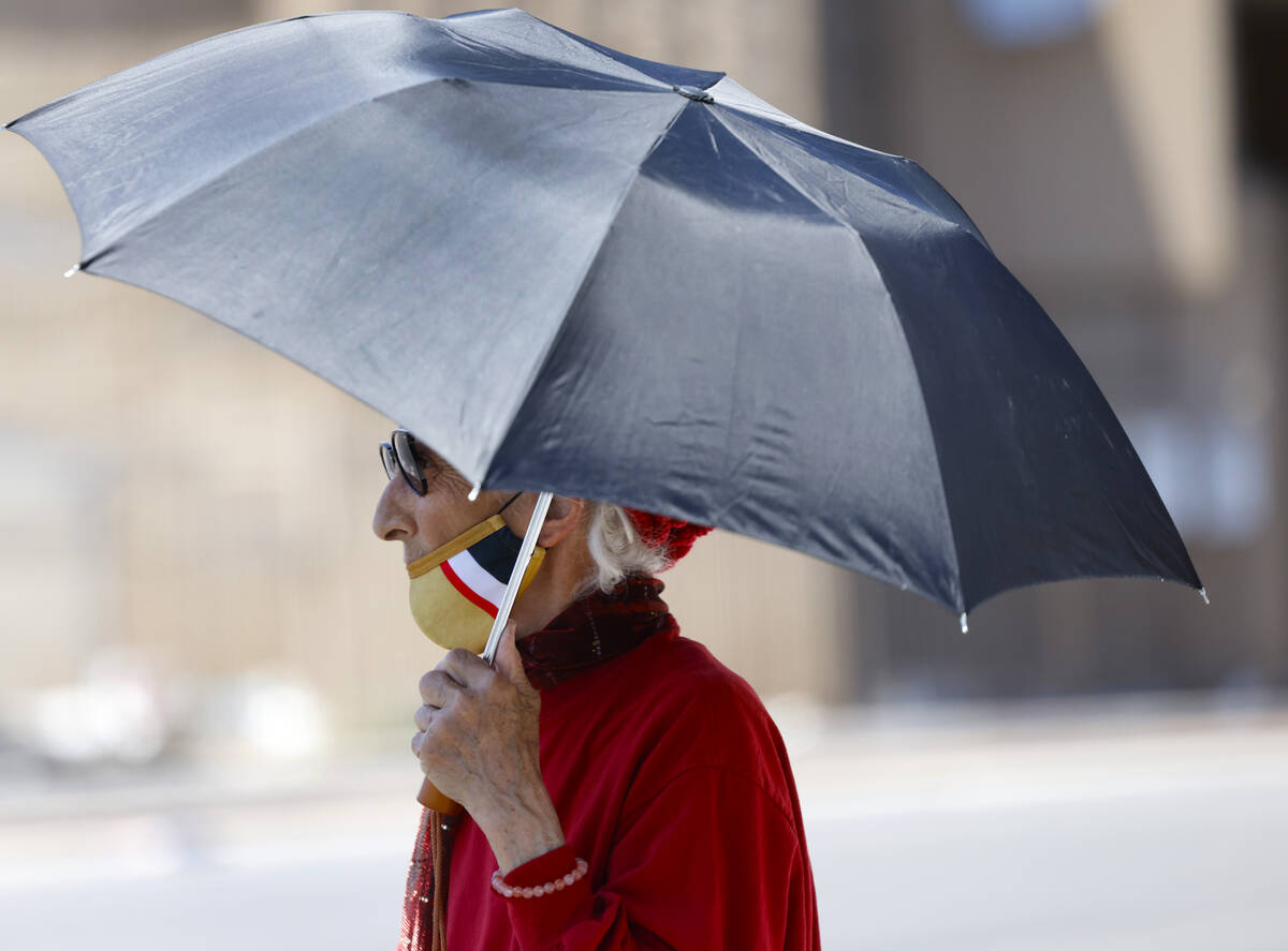 A pedestrian holds an umbrella to protect herself from sun as she walks along Main Street, on T ...