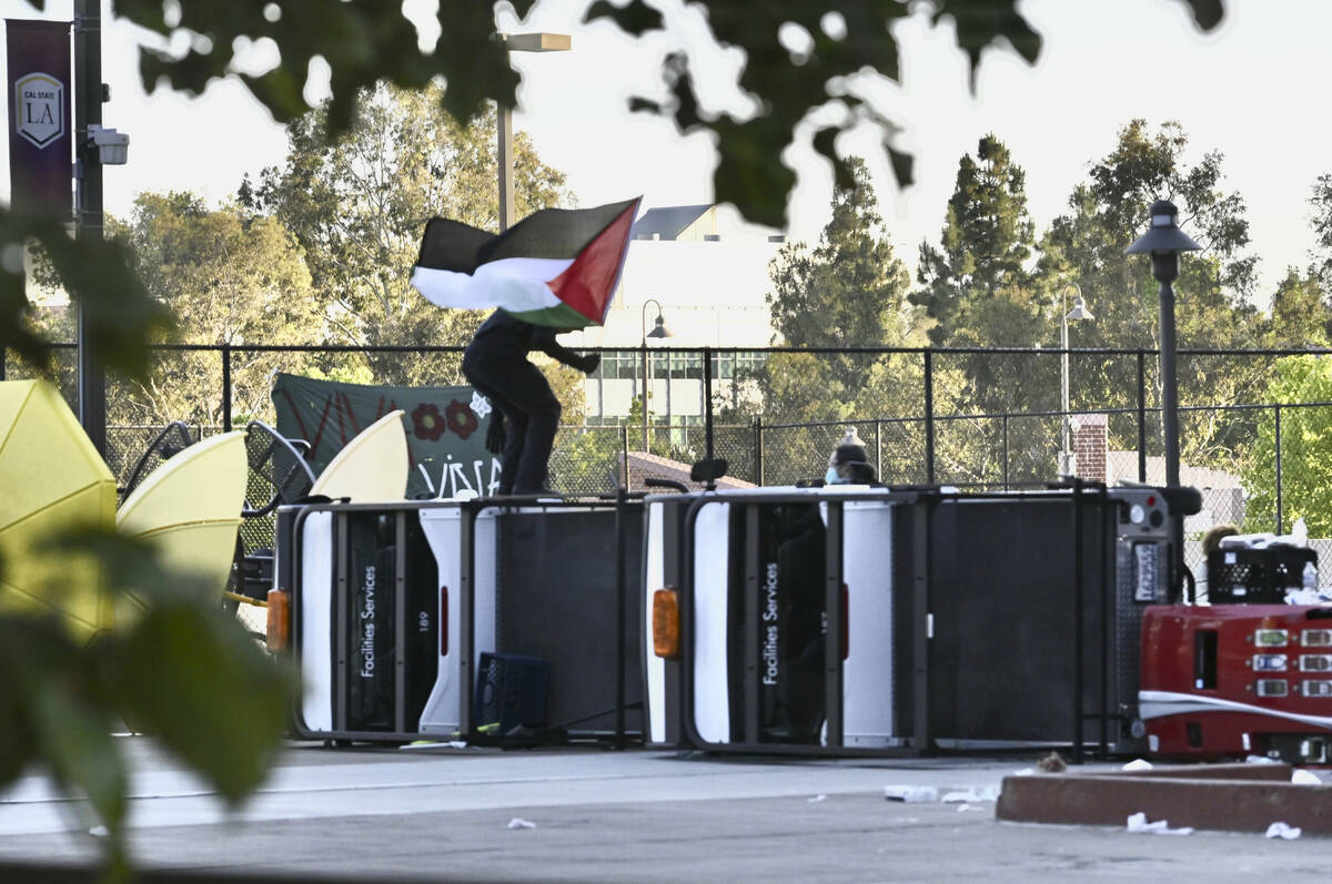 A pro-Palestinian student protester waves a Palestinian flag atop turned over utility carts whi ...