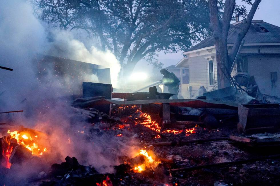 A firefighter sprays water on a burning outbuilding as the Point Fire spreads along West Dry Cr ...