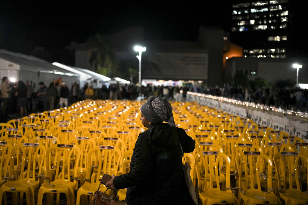 A woman walks by empty chairs tied together in an art installation depicting hostages held by H ...