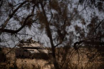 An Israeli soldier sits on the top of a tank near the Israeli-Gaza border, as seen from souther ...