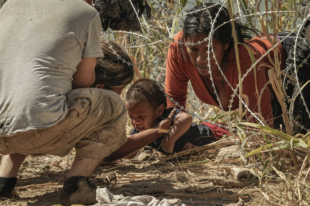 Migrants who crossed into the U.S. from Mexico pass under concertina wire along the Rio Grande ...