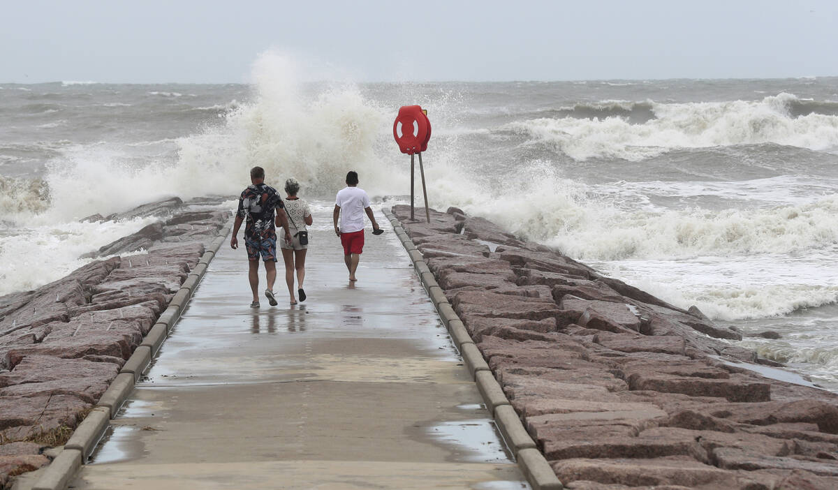 People watch waves crash into the 37th Street rock groin in Galveston, Texas on Sunday, July 7, ...