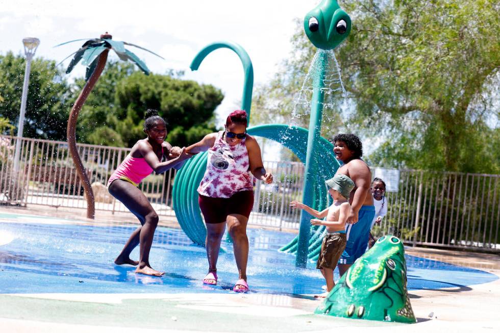 Garrus Williams, 4, center, watches as Markeisha Britton, second left, plays in the splash pad ...