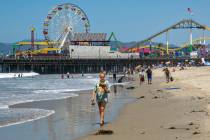 A woman reads a book as she walks on the beach near the Santa Monica Pier June 21, 2023, in San ...