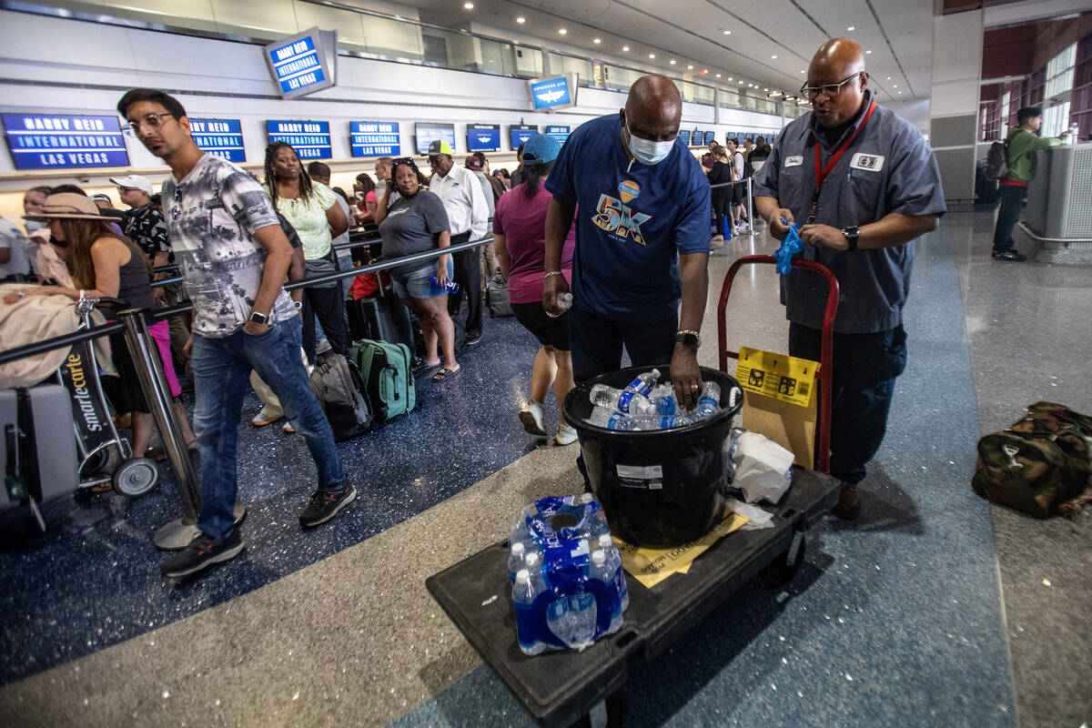 Workers hand out bottles of water at Harry Reid International Airport, Friday, July 19, 2024, i ...