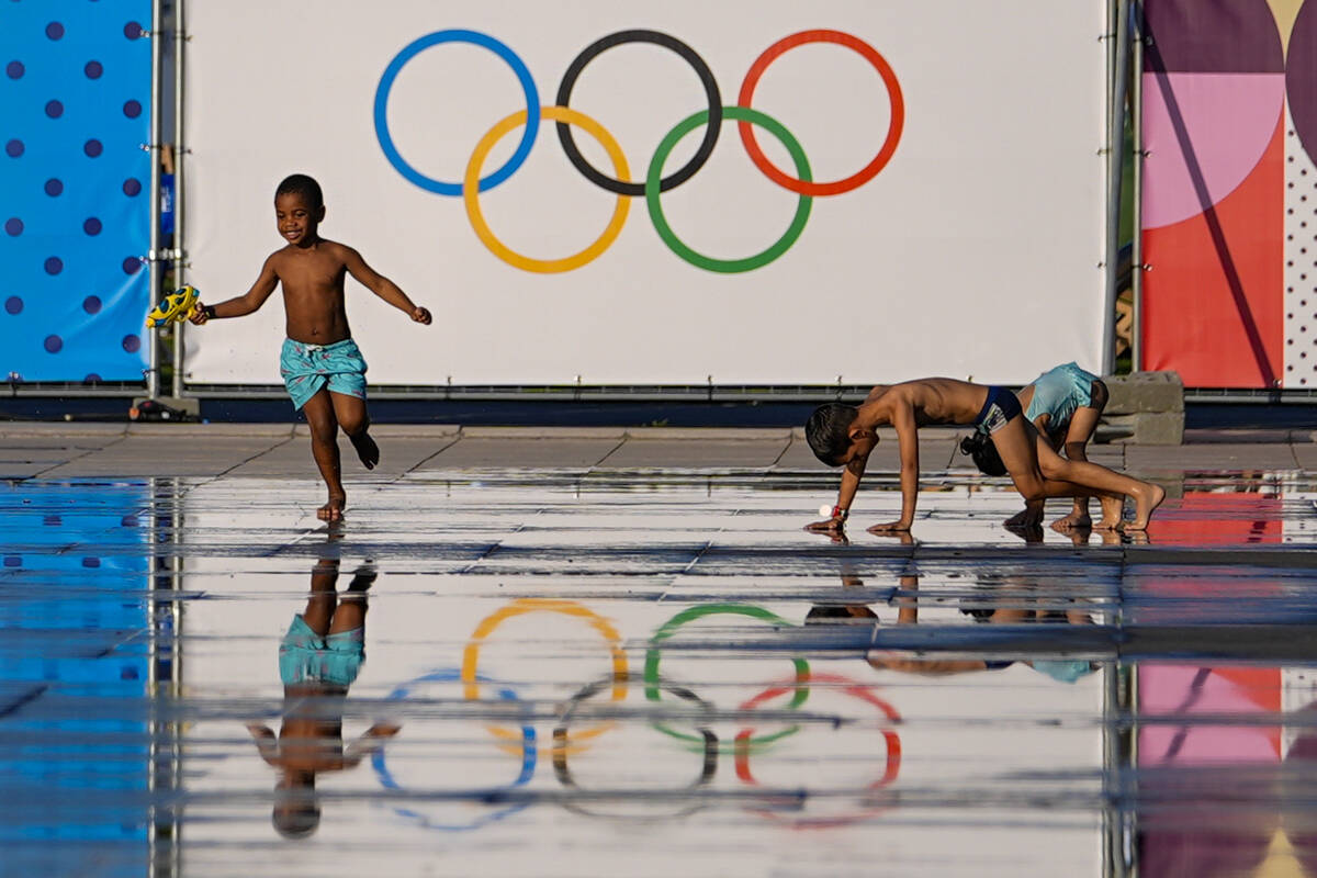 Children play at a splash fountain area near signage for the 2024 Summer Olympics, Tuesday, Jul ...