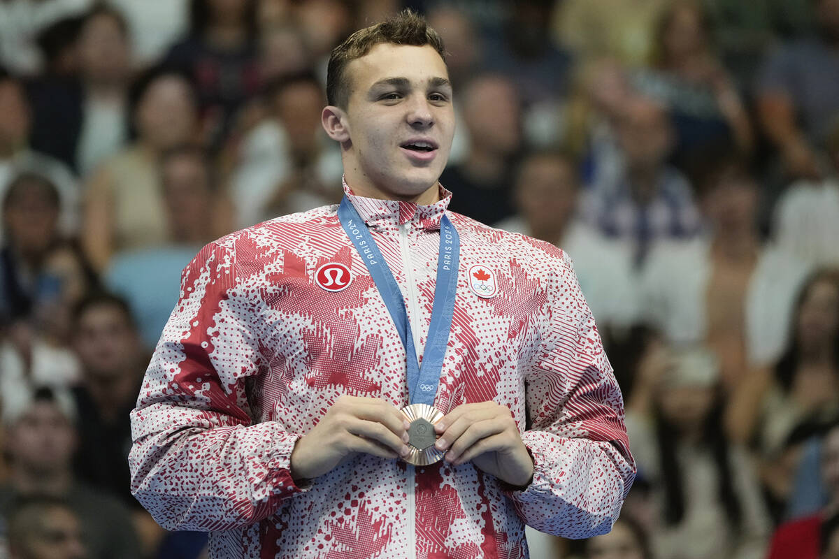 Canada's Ilya Kharun celebrates with the bronze medal on the podium for the men's 100-meter but ...