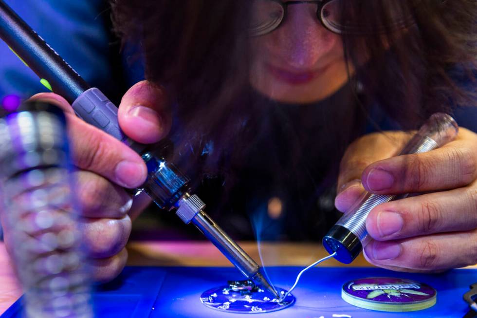 Attendee Forrest McMahon solders an electronic button in the HackerOne display during the Black ...