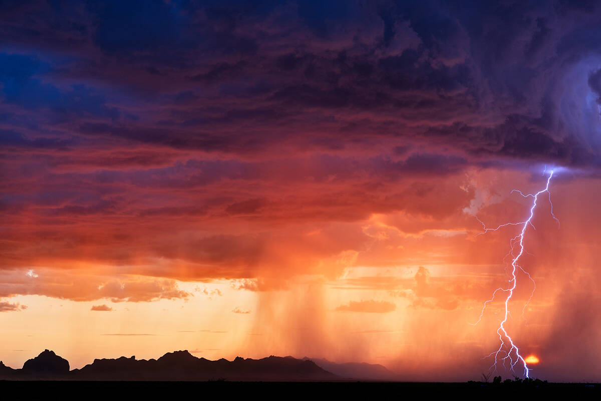 A lightning bolt strikes next to the setting sun as a thunderstorm moves through the desert nea ...