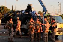 Lebanese army soldiers stand guard in front of a car that was hit by an Israeli strike as worke ...