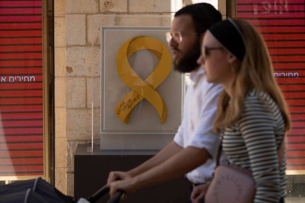 A couple stroll past artwork displayed in a pedestrian mall showing a yellow ribbon calling for ...