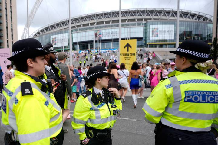 Police officers watch the arrival of Taylor Swift fans at Wembley Stadium in London, Thursday, ...