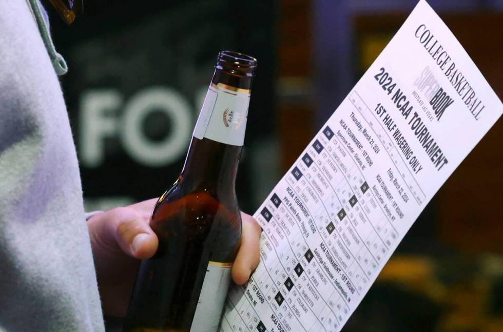 A man holds a betting sheet as he waits in line to bet on the NCAA basketball tournament at Wes ...