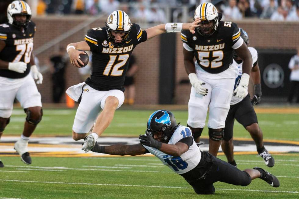 Missouri quarterback Brady Cook (12) leaps over Buffalo linebacker Dion Crawford (18) as he run ...