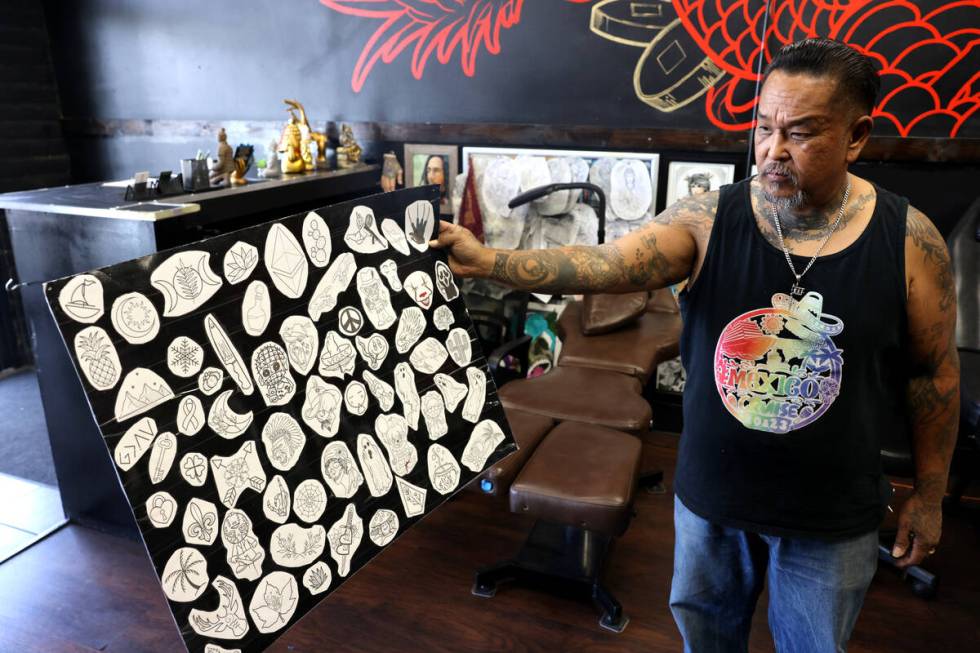 Monk, owner of The Iron Monk Tattoo Society, shows flash available for his shop’s Friday ...