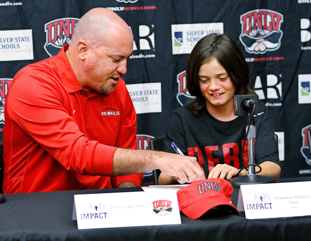 Thaddeus Thatcher, 9, who is battling cancer, signs with UNLV football coach Tony Sanchez durin ...