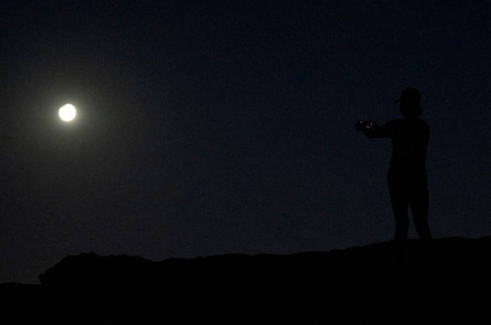 A woman takes a photograph during the Harvest Moon Supermoon partial lunar eclipse at Lone Moun ...