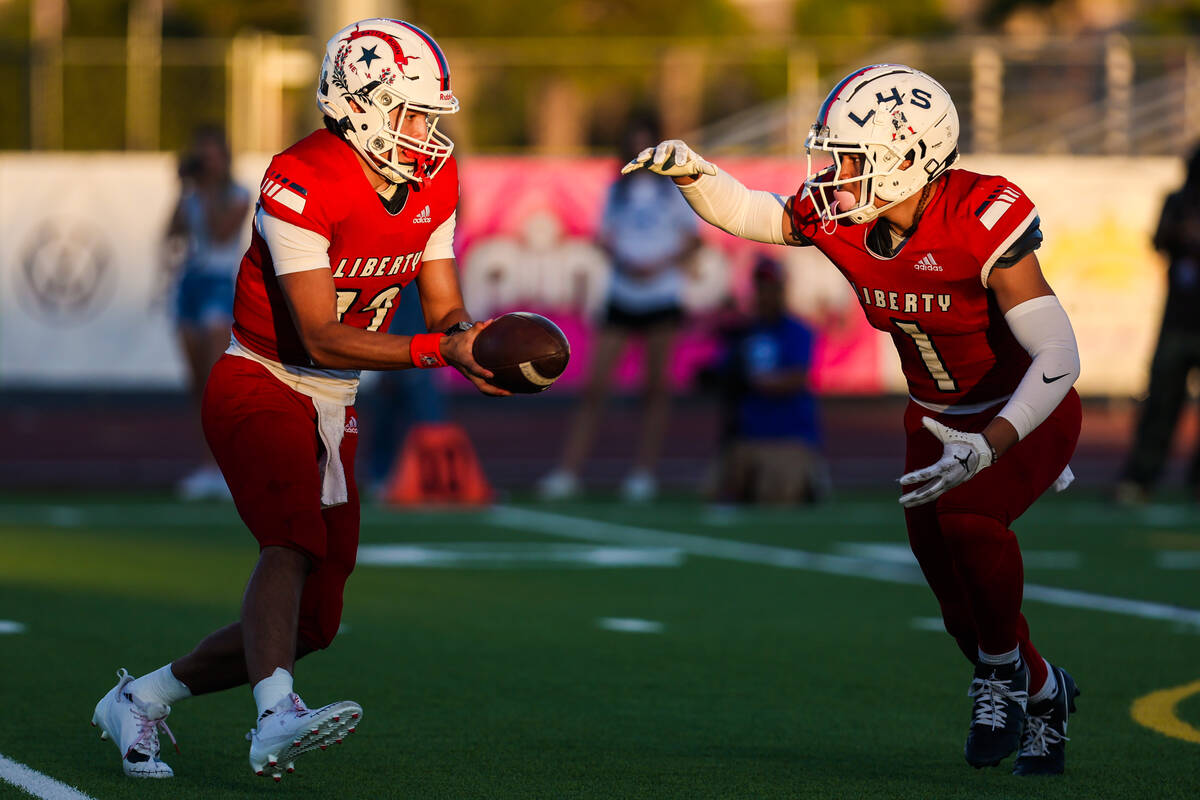 Liberty quarterback Elijah Espinoza (12) hands off the ball to running back Ezra Sanelivi (1) d ...