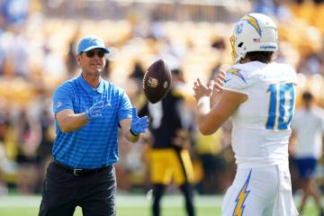 Los Angeles Chargers head coach Jim Harbaugh, left, tosses a ball to quarterback Justin Herbert ...