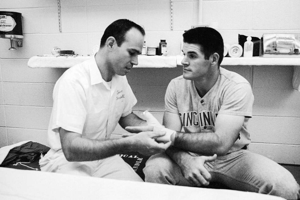 Trainer Bill Cooper, left, checks the bandage on the hand of Cincinnati star Pete Rose in the d ...