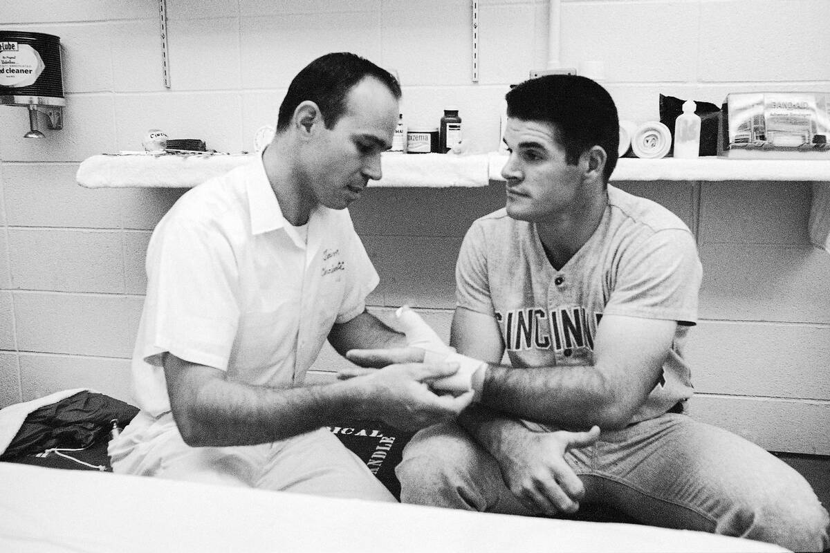 Trainer Bill Cooper, left, checks the bandage on the hand of Cincinnati star Pete Rose in the d ...