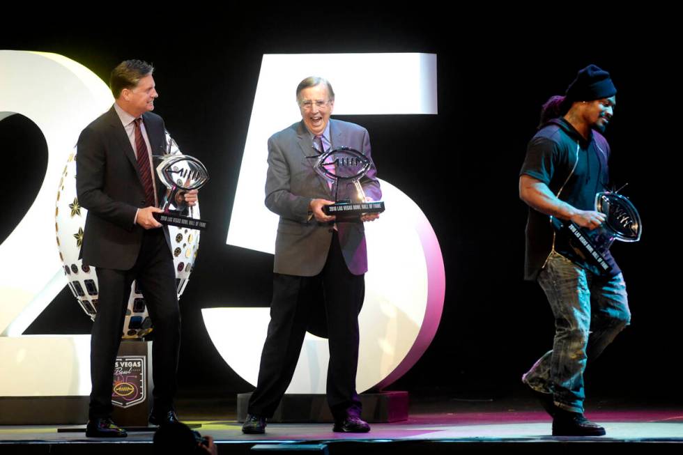 Brent Musburger laughs as Marshawn Lynch leaves the stage after quickly posing for photos with ...