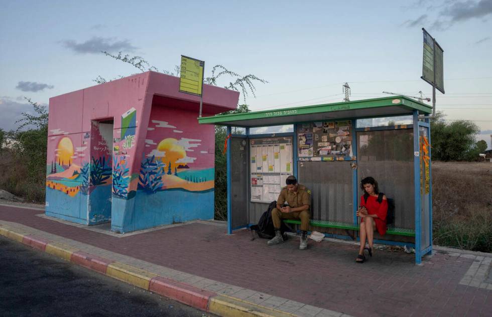 A soldier and a woman wait at a bus stop next to a bomb shelter in the town of Sderot, southern ...