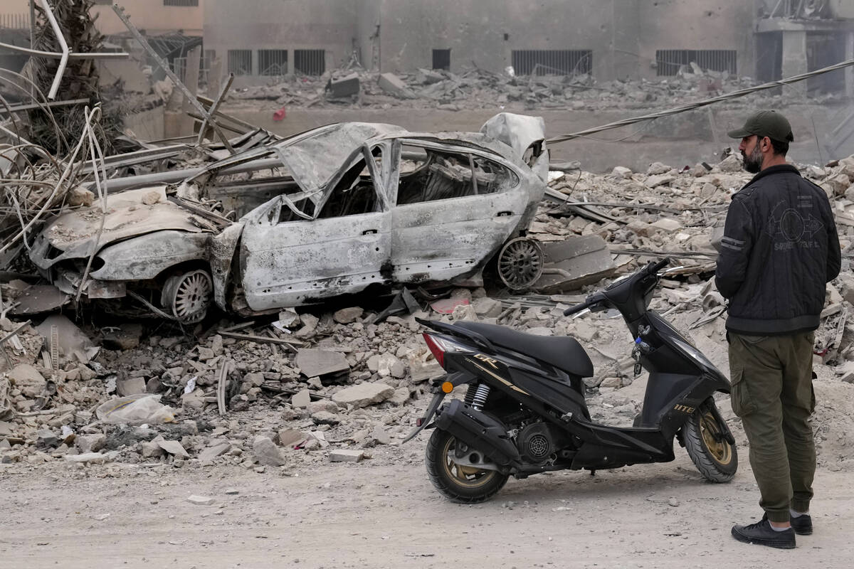 A man stands in front of a destroyed car at a scene hit by Israeli airstrikes in Dahiyeh, Beiru ...