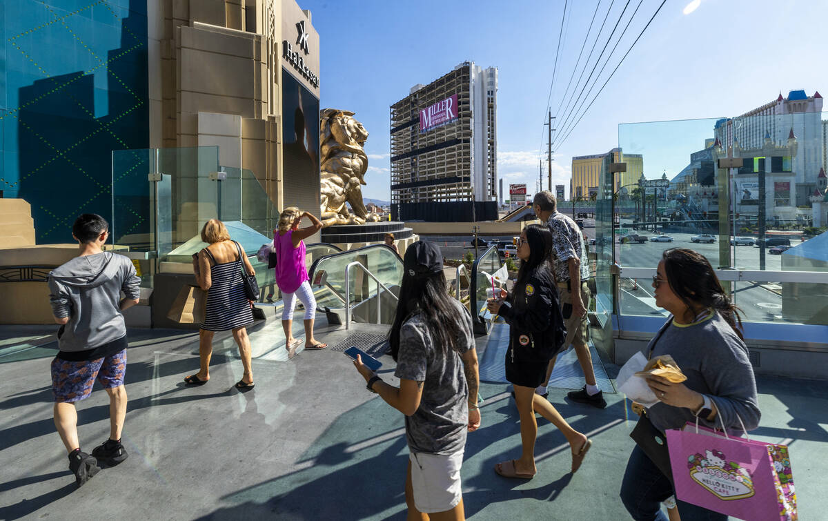 People walk about the MGM Grand pedestrian bridge while stealing a look at the Tropicana with i ...