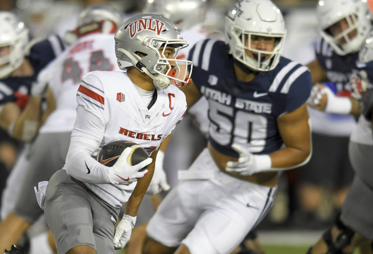 UNLV wide receiver Jacob De Jesus, left, carries the ball as Utah State defensive end Lawrence ...