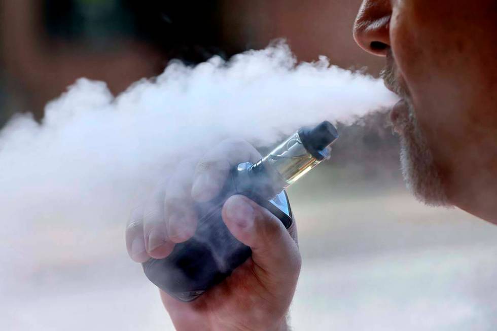 In this Aug. 28, 2019, file photo, a man exhales while smoking an e-cigarette in Portland, Main ...