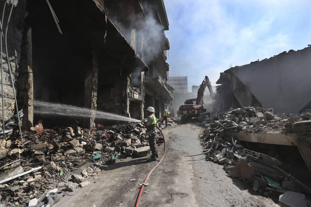 A Hezbollah firefighter hoses down on burned and destroyed shops at a commercial street that wa ...