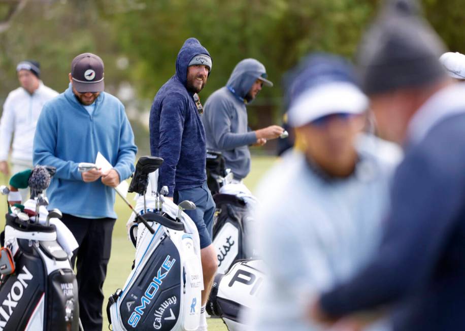 Players are bundled up to protect themselves from heavy wind as they practice teeing off at the ...