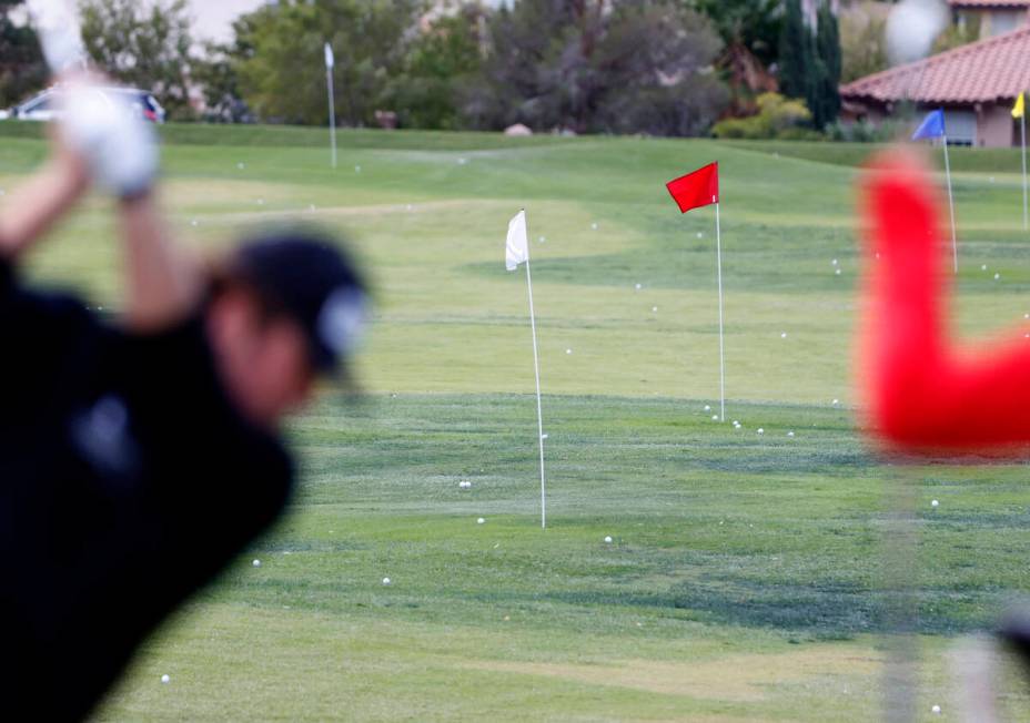 Players practice teeing off at the driving range as heavy wind blows small flags during the sec ...