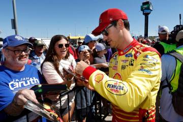 Joey Logano, right, gives autographs before a NASCAR Cup Series auto race at Kansas Speedway in ...