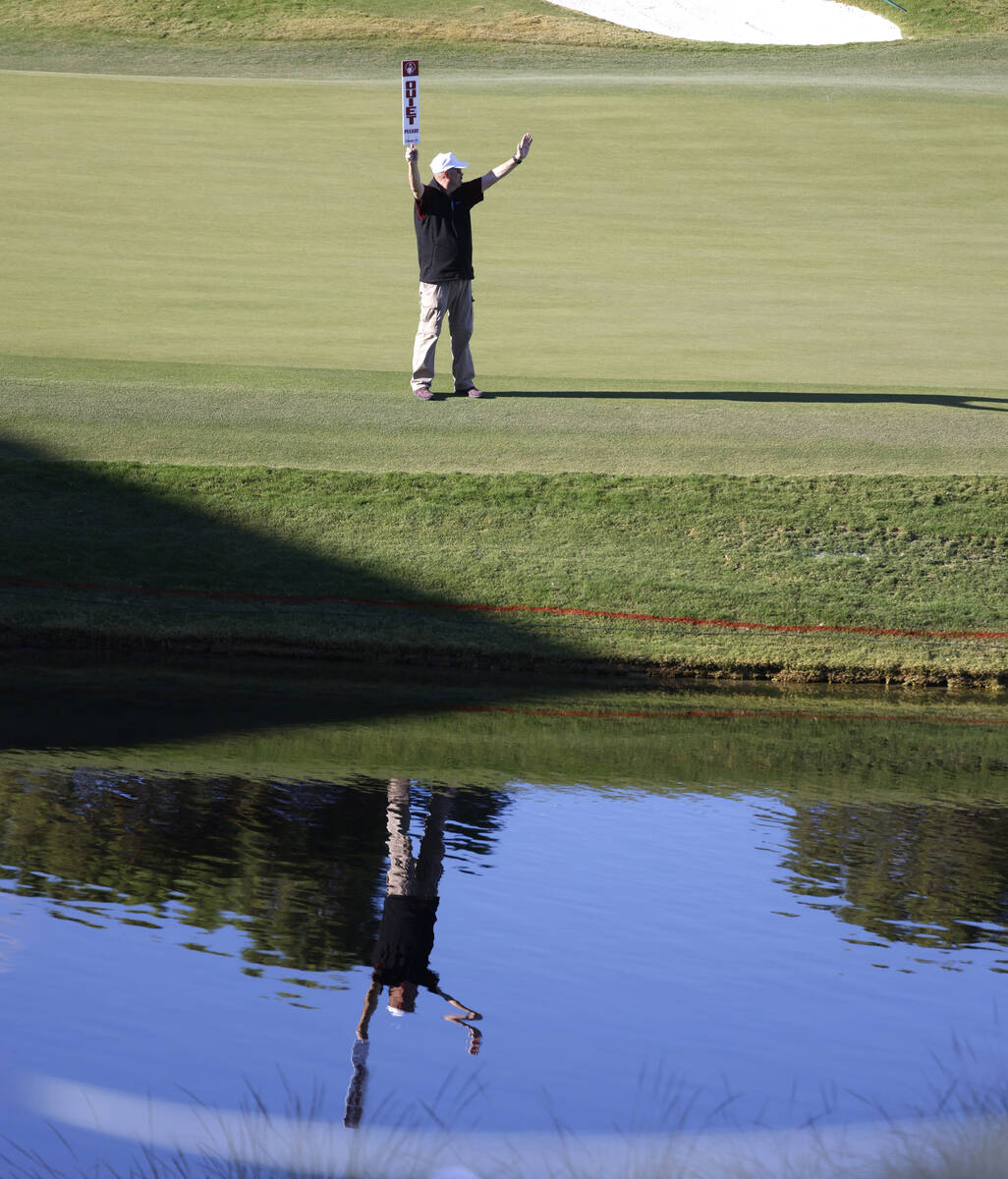 A volunteer is reflected in a pond as he holds a "Quiet" sign at green No.18 during t ...