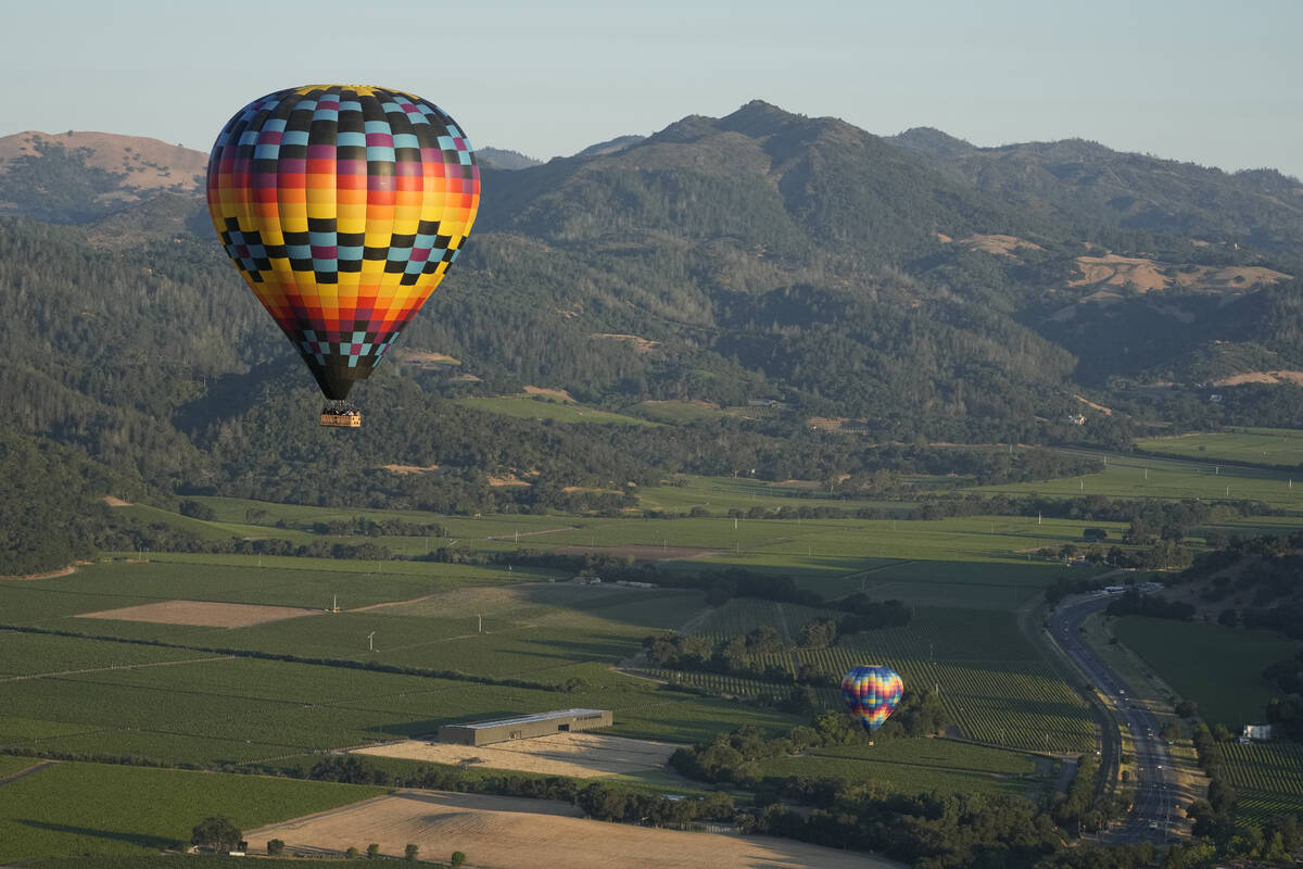 A pair of balloons make their way above the Dominus Estate winery and Highway 29, seen from a N ...