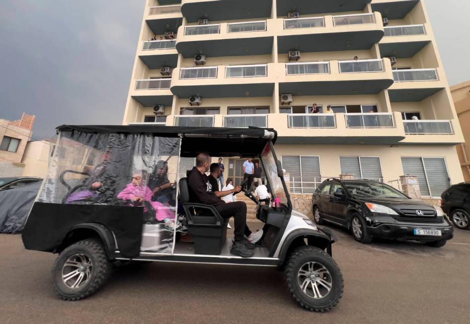 Residents ride a golf cart, as they pass in front of a building in Batroun, northern Lebanon, S ...