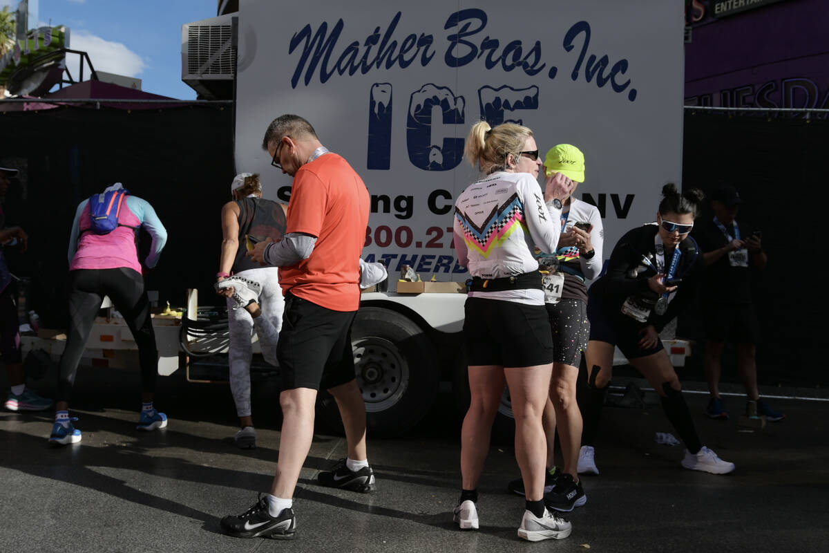 Participants stretch and check their phones after finishing the Las Vegas Marathon Sunday, Nov. ...