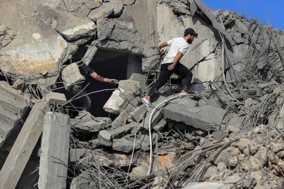 People search for victims at a destroyed building hit in an Israeli airstrike, in Ghaziyeh town ...