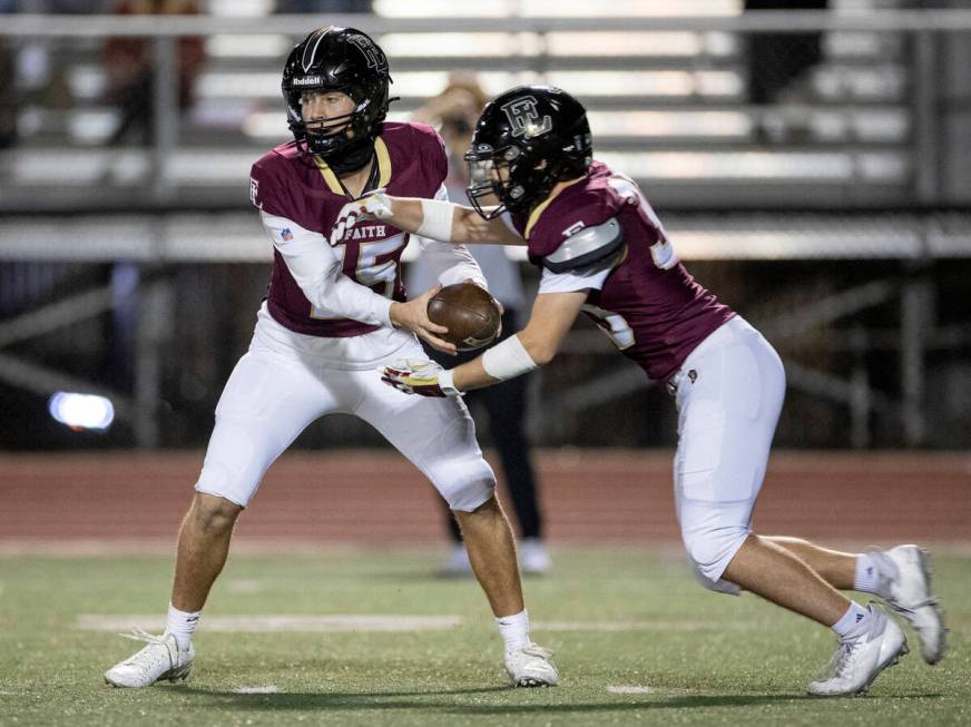 Faith Lutheran senior Alexander Rogers (15) hands the ball to junior Justin Robbins (33) during ...