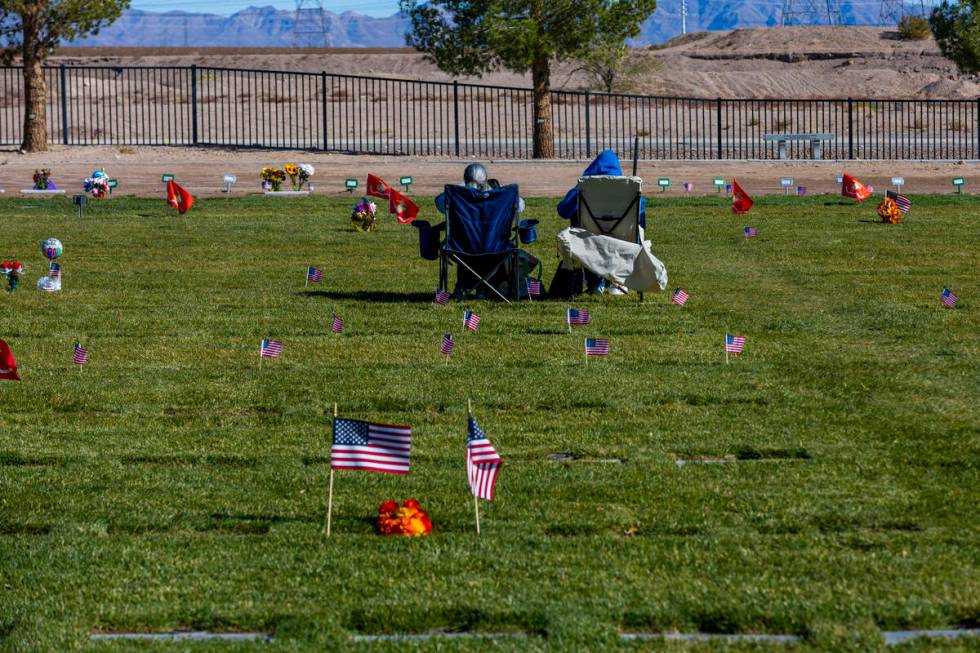 Visitors sit amongst a few of the 14,000 small American flags at veterans grave markers placed ...