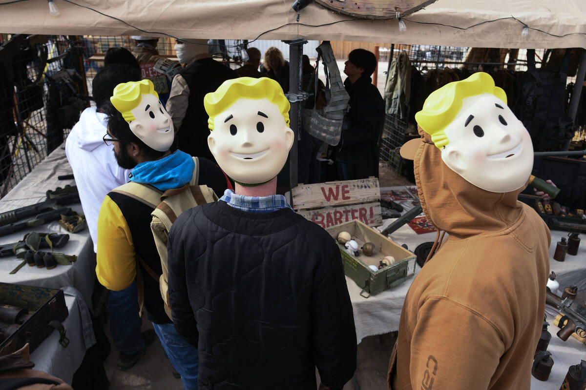 Attendees wear “Vault Boy” masks on their heads while shopping in the vendor area ...