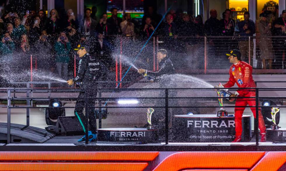 Mercedes driver George Russell and a team member spray champagne with Ferrari driver Carlos Sai ...