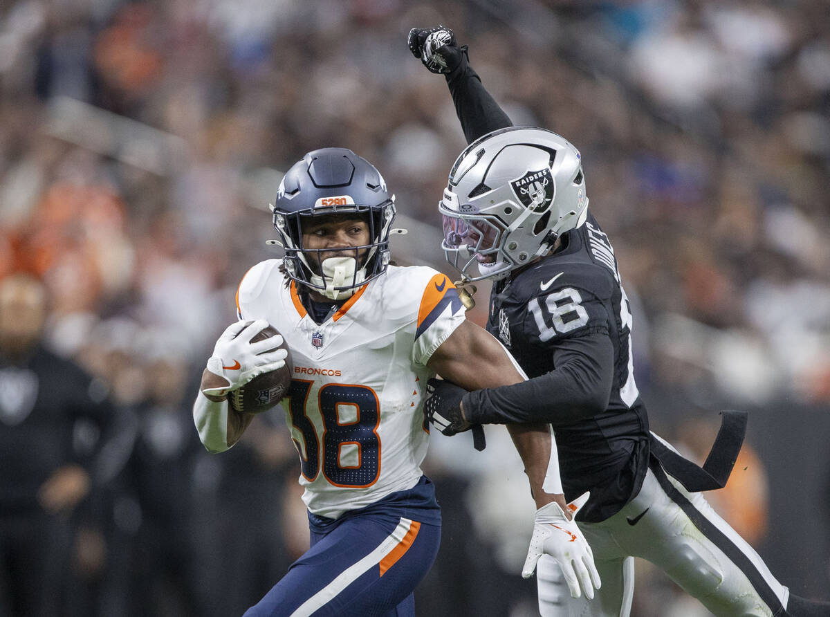 Raiders cornerback Jack Jones (18) attempts to punch the football out of Denver Broncos running ...